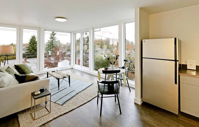 Living room with floor to ceiling windows with city and tree views. Staged with a couch, coffee table, rug and chair.at 19th & Mercer, Seattle Washington