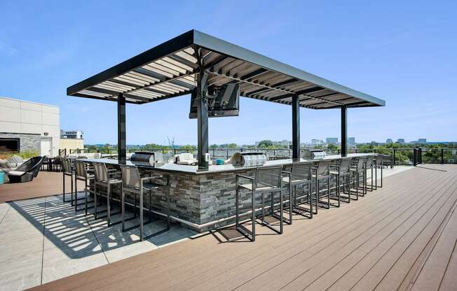 A wooden deck with a bar and chairs under a roof.