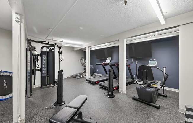 A gym with a variety of equipment including a rowing machine, a bench, and a treadmill.