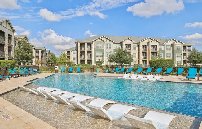 A swimming pool with lounge chairs and apartment buildings in the background.