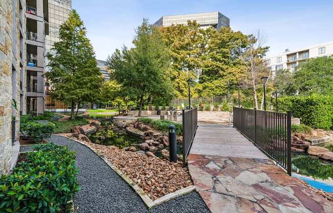 A walkway with a black fence and a gate leads to a rocky area with a pond.