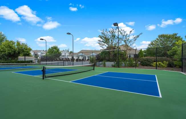 two tennis courts with houses in the background on a sunny day