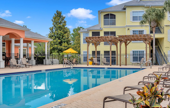 Pool with chaise lounges and pergola at Bermuda Estates Apartments in Ormond Beach, FL