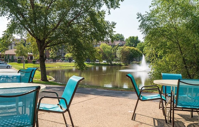 Outdoor patio with blue chairs, round tables, and a view of a lake with a fountain