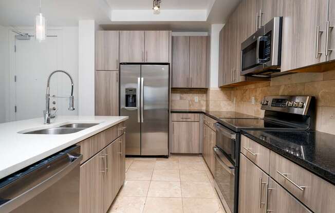 A kitchen with a stainless steel refrigerator and black countertops.