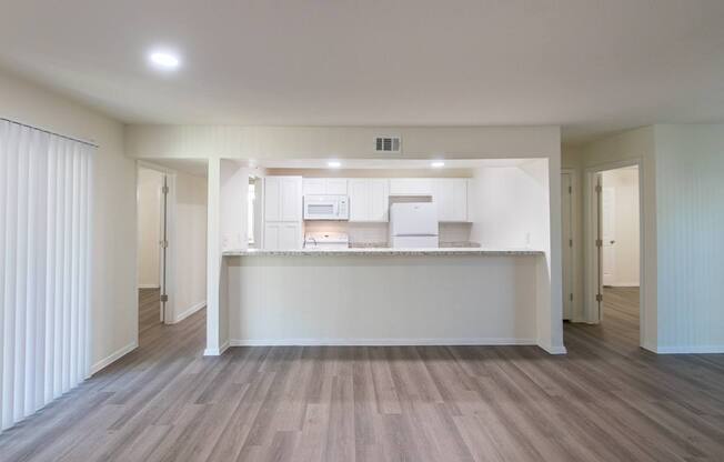 A kitchen with white appliances and cabinets with hardwoodlike flooring throughout viewed from the living room in a 2 bedroom, 2 bath 991 sq ft apartment home at The Biltmore Apartments located in the Vickery Midtown neighborhood of Dallas, TX.