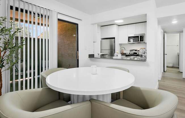 A modern kitchen with a white table and beige chairs.