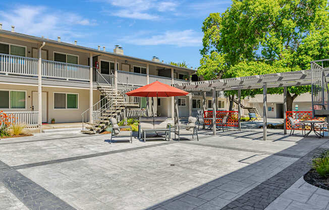 A patio area with a red umbrella and chairs.