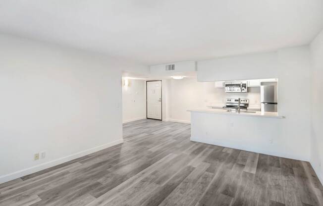 the living room and kitchen of an apartment with white walls and wood flooring