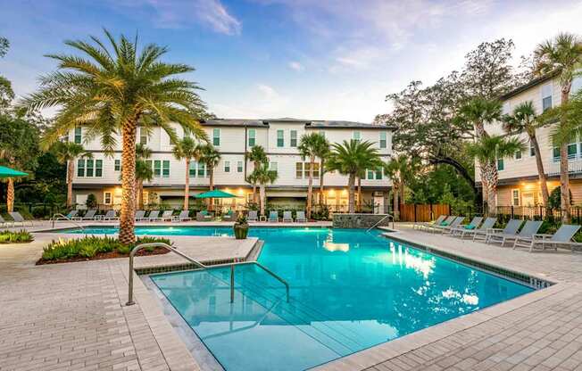 A swimming pool surrounded by lounge chairs and palm trees in front of a hotel.