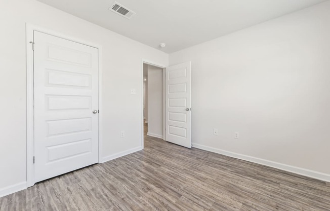 the living room and bedroom of a manufactured home with white walls and wood flooring