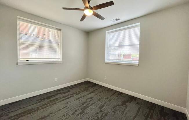 A room with a ceiling fan and two windows.