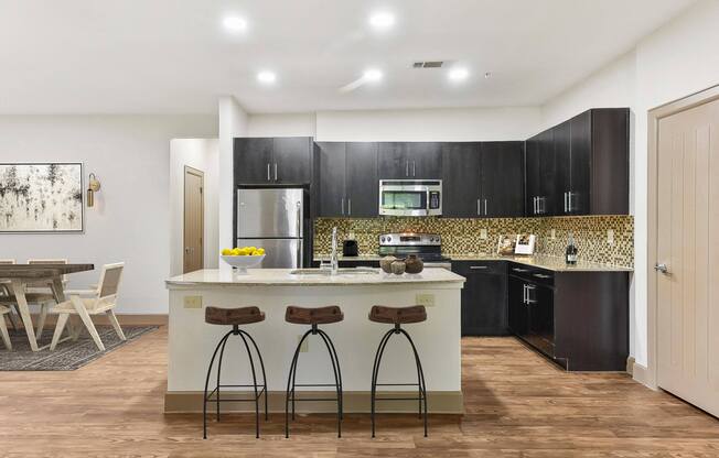 a kitchen with black cabinets and a counter with three stools at Lakeline East Apartments, Cedar Park, TX