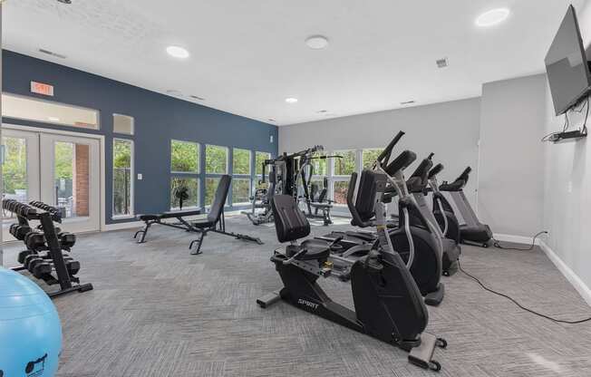 an exercise room with cardio equipment in a building with windows