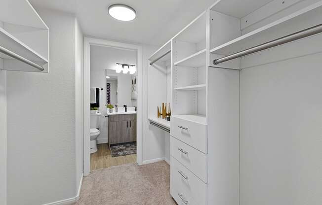 a walk in closet with white cabinets and a bathroom with a toilet and a sink