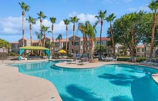 a resort style swimming pool with chaise lounge chairs and palm trees in the background