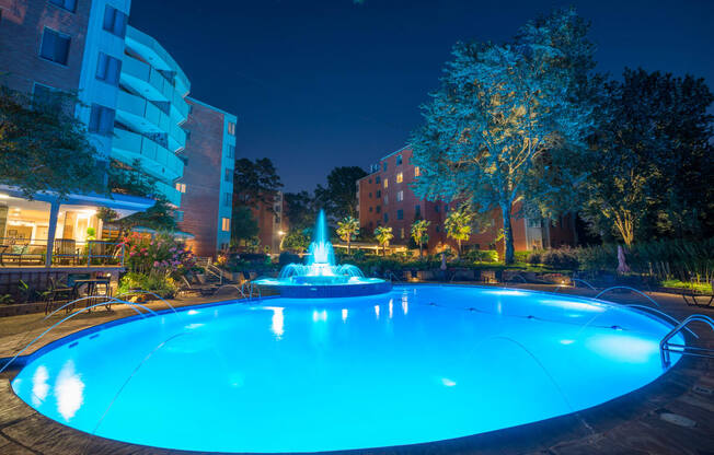 a swimming pool with a fountain in front of a building at night