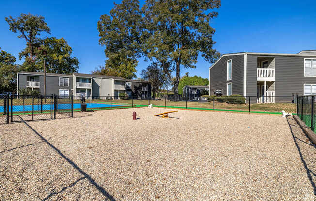 A dog park with a sandy area and a fence in front of apartment buildings at Maplewood apartments in Shreveport, LA.