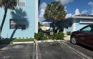 A red car is parked in a parking lot in front of a blue building.