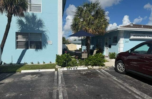 A red car is parked in a parking lot in front of a blue building.