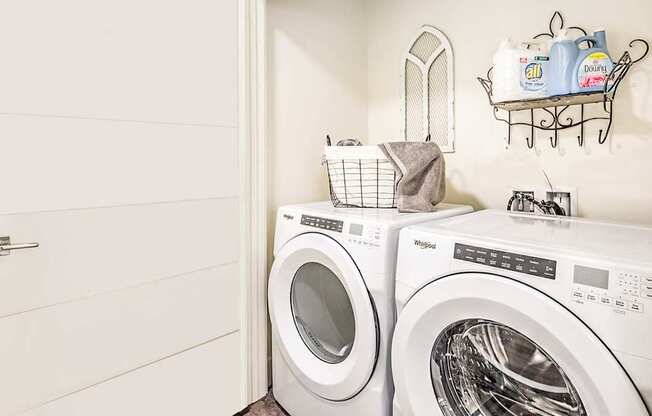 A white laundry room with two washing machines and a basket on top of one of them.