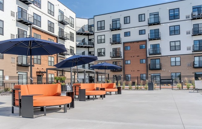 A sunny day at a modern apartment complex with orange seating and umbrellas.