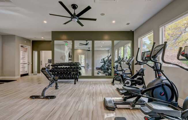 a gym with cardio machines and a ceiling fan