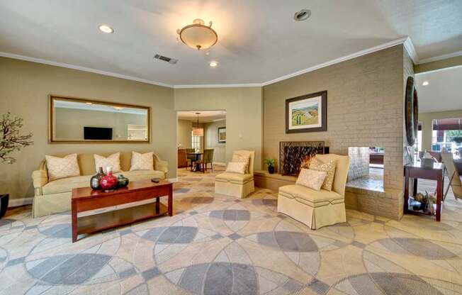A comfortable community living area here at Trinity Place with plush seating arranged around a wooden coffee table. Neutral-toned carpet and soft lighting create a relaxed atmosphere, while a decorative fireplace adds a cozy focal point. An open layout connects to nearby lounge and dining spaces, making it ideal for gathering and everyday use.