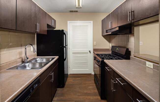 A kitchen with dark brown cabinets and a black fridge.
