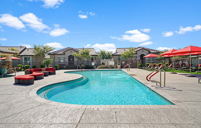 a swimming pool with red chairs and umbrellas and apartments in the background