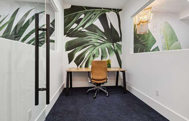 A room with a desk and a chair with a leafy wallpaper.