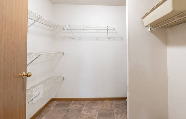 an empty closet with white walls and an open door to a white closet with shelves. Fargo, ND Oxford Apartments