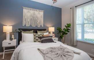 A bedroom with a white bed and a white nightstand with a lamp on it.