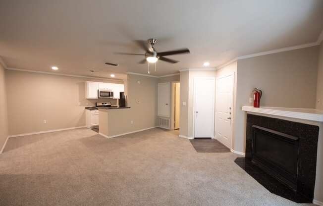 View of Tuscany from living area with carpet flooring, gas fireplace, ceiling fan and view of kitchen with white cabinets, dark counters, and stainless appliances.