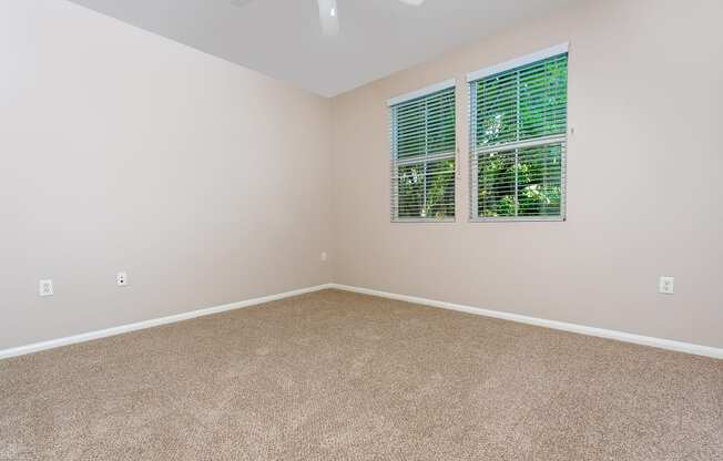 a bedroom with beige carpet and two windows