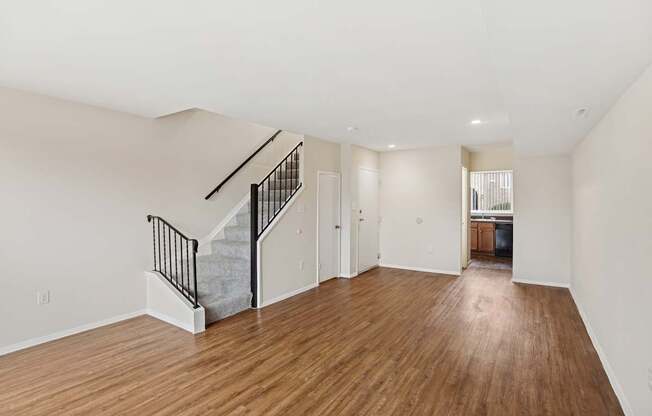 A spacious room with wooden floors and a staircase with a metal railing.