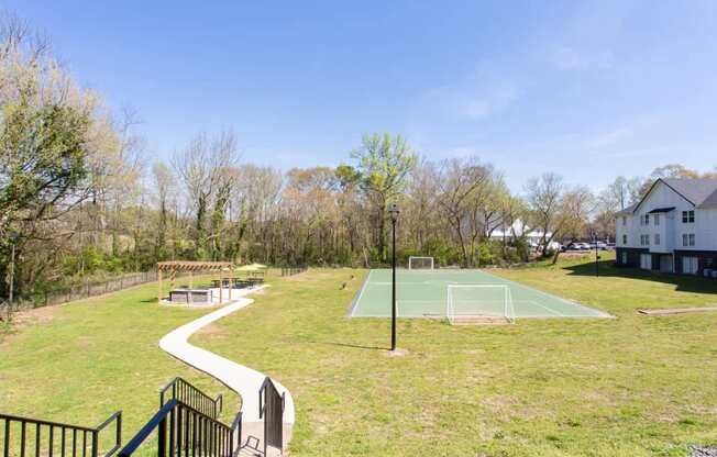 A green grassy area with a basketball court and a house in the background.