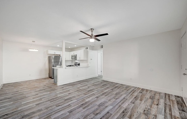 A room with a ceiling fan and a kitchenette in the background.
