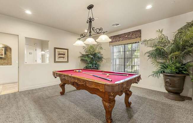 A pool table in a room with a chandelier and potted plants.