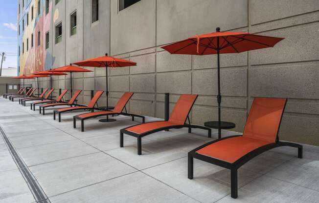 a row of orange lounge chairs with red umbrellas in front of a building  at The Icon, Richmond, VA