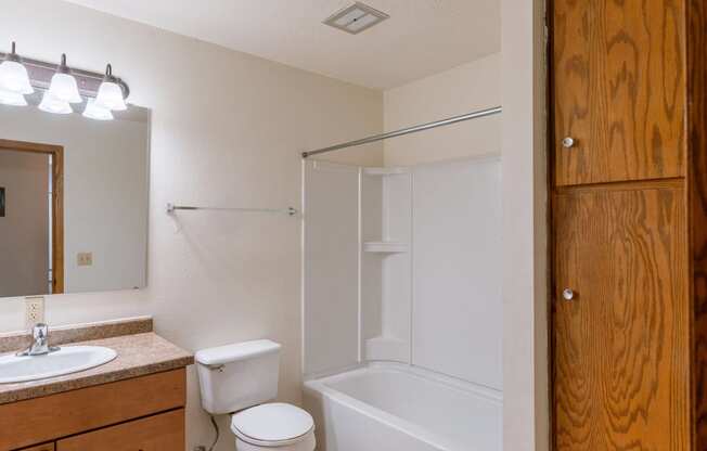 a bathroom with a shower toilet and sink and a mirror. Fargo, ND Schrock Apartments