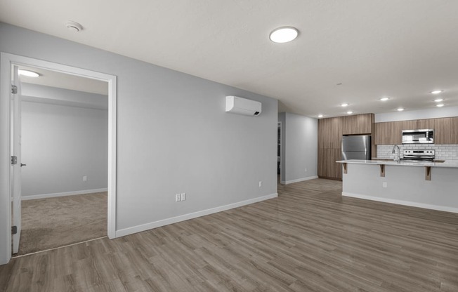 an empty living room and kitchen with wood flooring and white walls