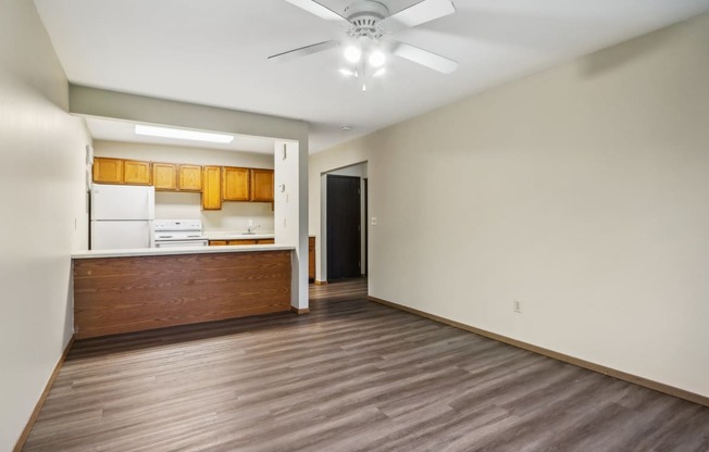 a empty living room with a kitchen and a ceiling fan