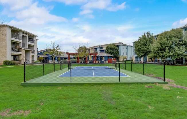 A tennis court is surrounded by apartment buildings.