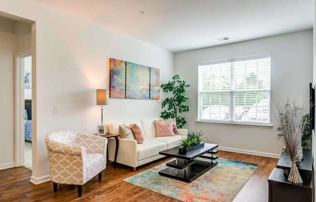 A living room with a white couch, a chair, a coffee table, and a painting on the wall.