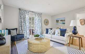 A living room with a white couch, a round wicker table, and a painting on the wall.