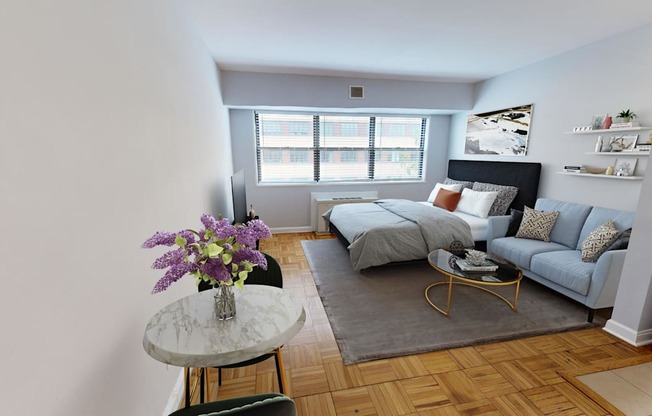 A living room with a grey couch, a round table with flowers, and a window.