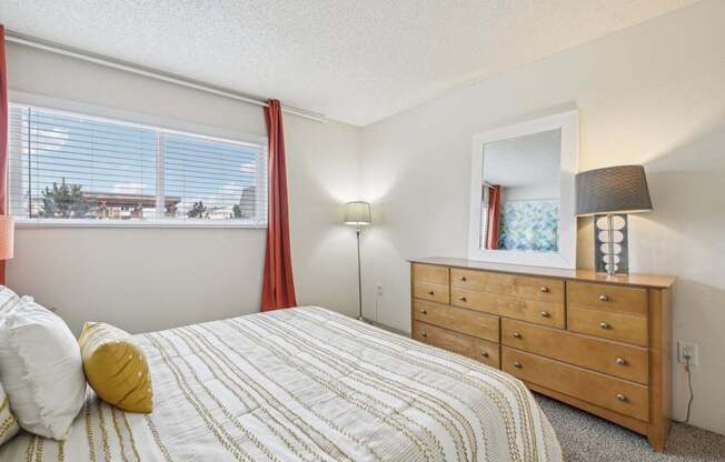 A bedroom with a bed, dresser, and window with red curtains.
