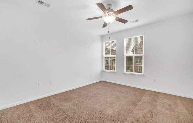 an empty living room with a ceiling fan and two windows