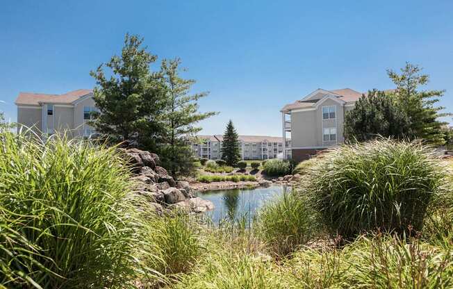 A serene landscape with a pond, houses, and lush greenery.